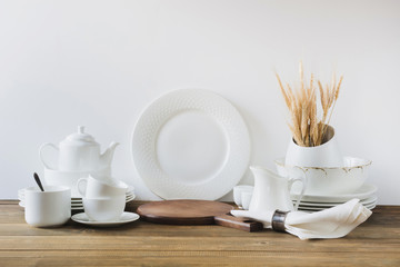 White kitchen utensils, dishware and other different white stuff for serving on white wooden board.