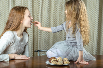 baby with long hair in a puffy skirt feeds oatmeal cookies to an older teenage girl
