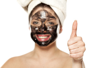 Young happy woman with towel on her head posing with black mask on her face