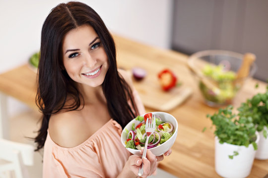 Happy woman preparing salad in modern kitchen