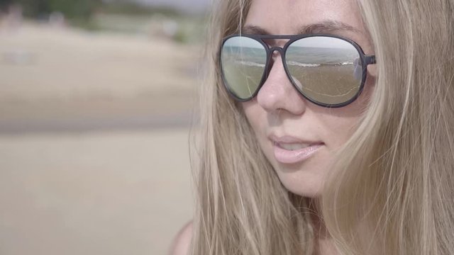 Close up portrait of beautiful young blonde woman in sunglasses enjoying view of tropical beach slow motion