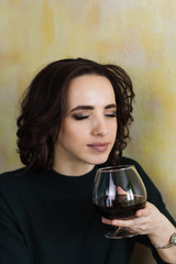 beautiful woman with closed eyes holds a glass of red wine and inhales its aroma