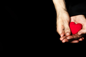 Palm of a peasant woman with plush red heart on a black fabric.
