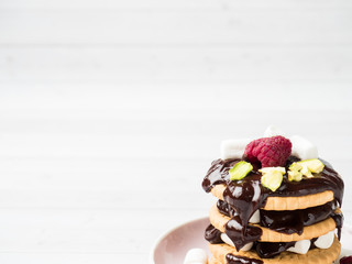A sweet dessert of a chocolate cookie raspberry and marshmallow on a light table.