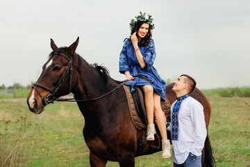 Fototapeta premium The charming smile of a girl who elegantly sits in a saddle on a horse and her boyfriend looks at her