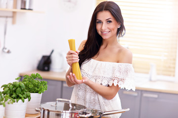 Young woman trying to prepare pasta in kitchen