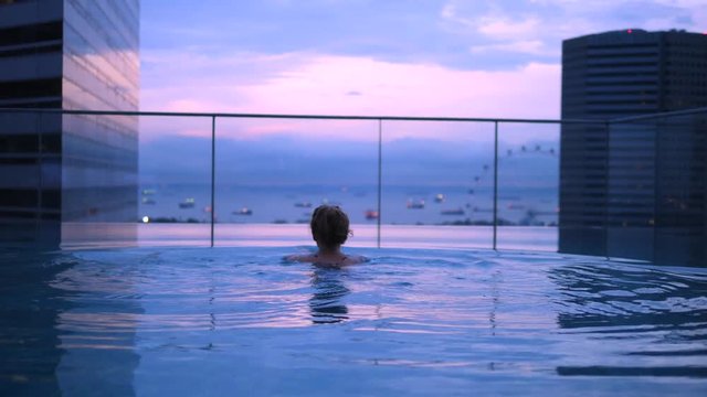 Woman Relaxing In Infinity Swimming Pool Enjoying City View