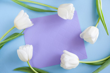 Five white tulips are lying in a circle around lilac sheet on blue background.