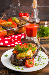Eggplants stuffed with minced meat and cooked with fresh tomatoes and bell peppers on white plate and in baking dish on wooden rustic table.