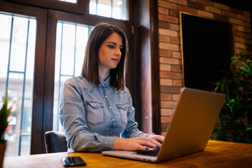 Smiling female copywriter working remote at laptop device connecting to wireless internet.Attractive female freelancer wit good mood chatting in social networks with friend sitting in coffee shop