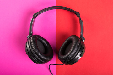 One pair of black headphones on pink and red background.