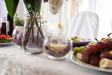 Beige candle in a glass vase with lilac petals. Wedding decor on the table at the newlyweds