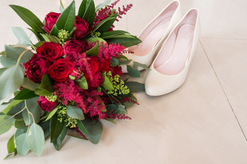 Lush bridal Bouquet of red roses and a lot of greenery with elegant bridal shoes. Wedding details 