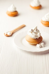 Cupcakes with vanilla cream and marshmallow on white plate, on wooden backdrop, vertical composition