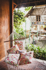 Hammock with colorful pillows hanging in hipster wooden house. Place for relax, tropical mood