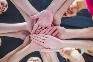 Close up photo of young smiling women putting their hands together. Friends with stack of hands showing unity and teamwork.
