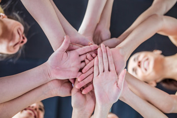 Close up photo of young smiling women putting their hands together. Friends with stack of hands showing unity and teamwork.