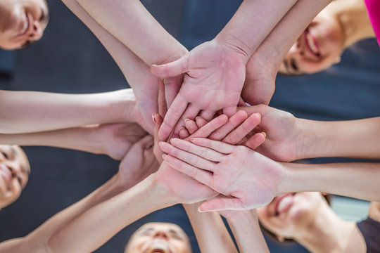 Close up photo of young smiling women putting their hands together. Friends with stack of hands showing unity and teamwork. © My Ocean studio