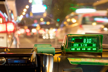 The digital taxi meter on the dashboard of cab shows kilometer and cost. Night taxi ride in traffic...