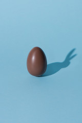 One chocolate easter egg with bunny shadow on blue surface