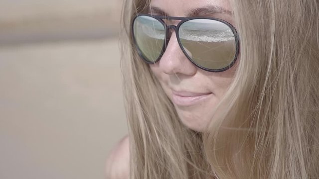 Close up portrait of beautiful young blonde woman in sunglasses enjoying view of tropical beach slow motion