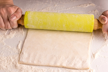 Woman rolls puff pastry on a light table, floured