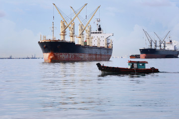 Small passenger boat running in the sea and have cargo ship.