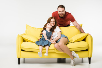 Mother and daughter on sofa while father standing behind isolated on white