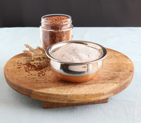 Ragi flour, which is gluten-free, in a bowl, and in the background is a bottle with ragi, which is also known as finger millet, and dried stalks. © Greentree