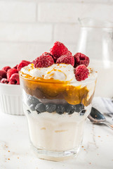 Healthy breakfast, semolina porridge pudding in glass with milk, cream, caramel and berries, white marble table copy space