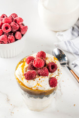 Healthy breakfast, semolina porridge pudding in glass with milk, cream, caramel and berries, white marble table copy space