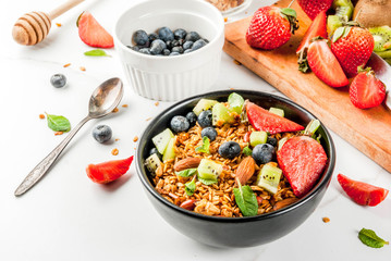Healthy breakfast with muesli or granola with nuts and fresh berries and fruits - strawberry, blueberry, kiwi, on white table, copy space