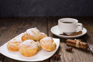 Delicious eclairs sprinkled with icing sugar, stand on a wooden table. Copy spase.