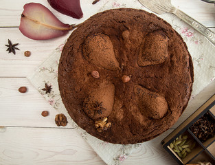 Chocolate cake with pears stewed in red wine, hazelnuts, walnuts on white wooden background. Traditional dessert. Top view.