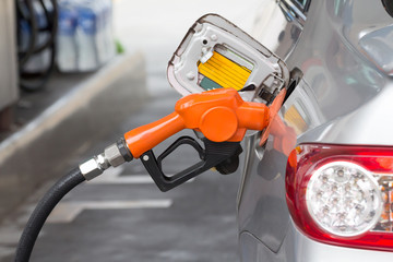 fuel nozzle is filling oil to silver car at petroleum station,  refill     oil fuel.  concept : Use of mobile phones at petrol stations do not cause fires