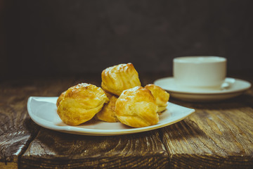Delicious eclairs sprinkled with icing sugar, stand on a wooden table. Copy spase.