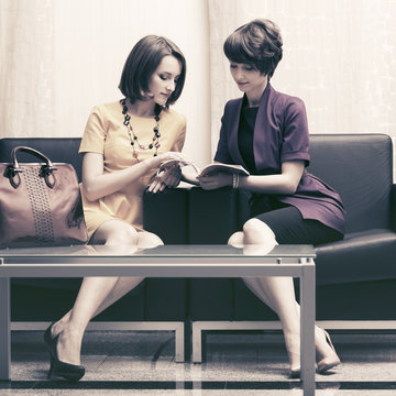 Two young fashion business women sitting on couch in showroom