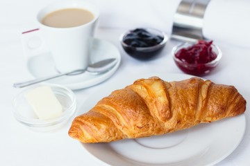 Croissant breakfast served with jams, butter and a cup of coffee with milk