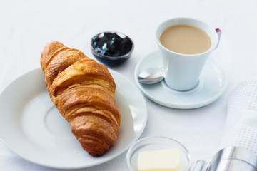 Hotel style breakfast of fresh crispy croissant, cup of coffee, butter and blueberry jam