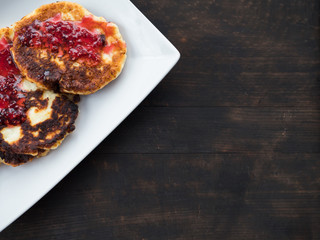 pancakes, cheesecakes with raspberry jam on a white plate, dark background
