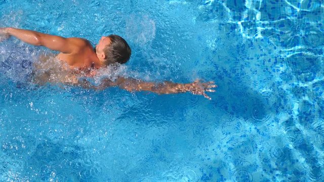 Top view of sporty man swimming in clear blue water of basin. Unrecognizable young sporty guy floating across the pool of hotel on sunny day. Concept of summer vacation or holiday. Close up