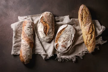 Tuinposter Variety of loafs fresh baked artisan rye and whole grain bread on linen cloth over dark brown texture background. Top view, copy space. © Natasha Breen