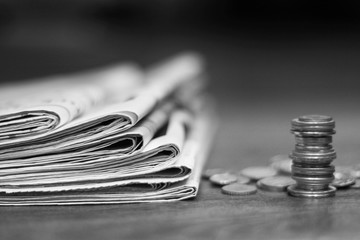 News and finance. Folded newspapers and stacked coins on table. Concept for business and financing. Daily papers with actual information and different money cash.
