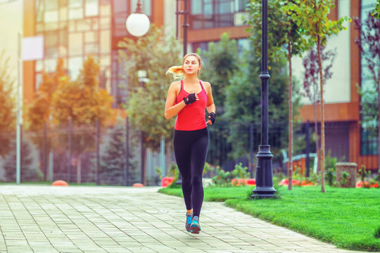 A beautiful sporty woman runing on street in sportswear. Training sun day