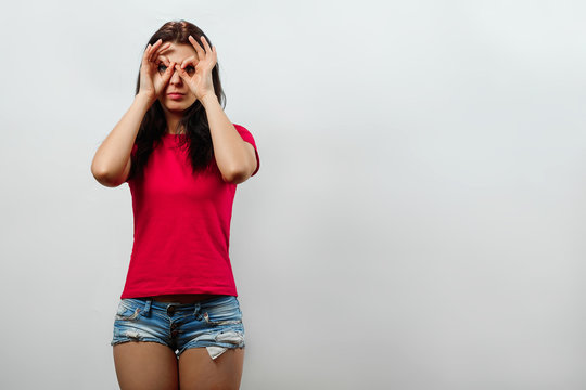 Young, beautiful girl makes binoculars out of hands, visionary. Isolated on a light background. Different human emotions, feelings of facial expression, attitude, perception, body language, reaction.