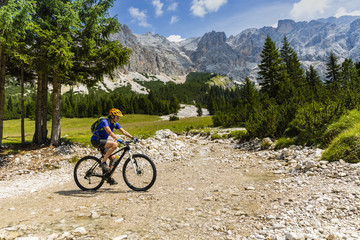 Fototapeta premium Turystyczna jazda na rowerze w Cortina d'Ampezzo, w tle wspaniałe góry skaliste. Kobieta na rowerze górskim enduro. Prowincja Południowego Tyrolu we Włoszech, Dolomity.