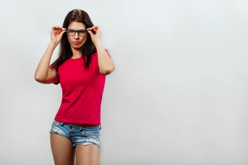 A young, beautiful girl adjusts her glasses. Isolated on a light background. Different human emotions, feelings of facial expression, attitude, perception, body language, reaction.