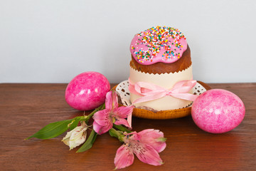  Easter still life with traditional holiday food: home cake with sweet icing and pink bright eggs on a wooden table. Empty space for text