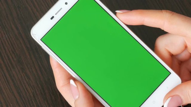 Female hands with beautiful French manicure take a white smartphone with Green Screen. Using Smartphone,Holding Smartphone with Green Screen