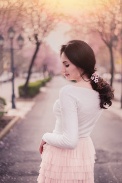 Female portrait in blooming cherry tree street in Tirana Albania, calm pastel peach colours and sun flare in background